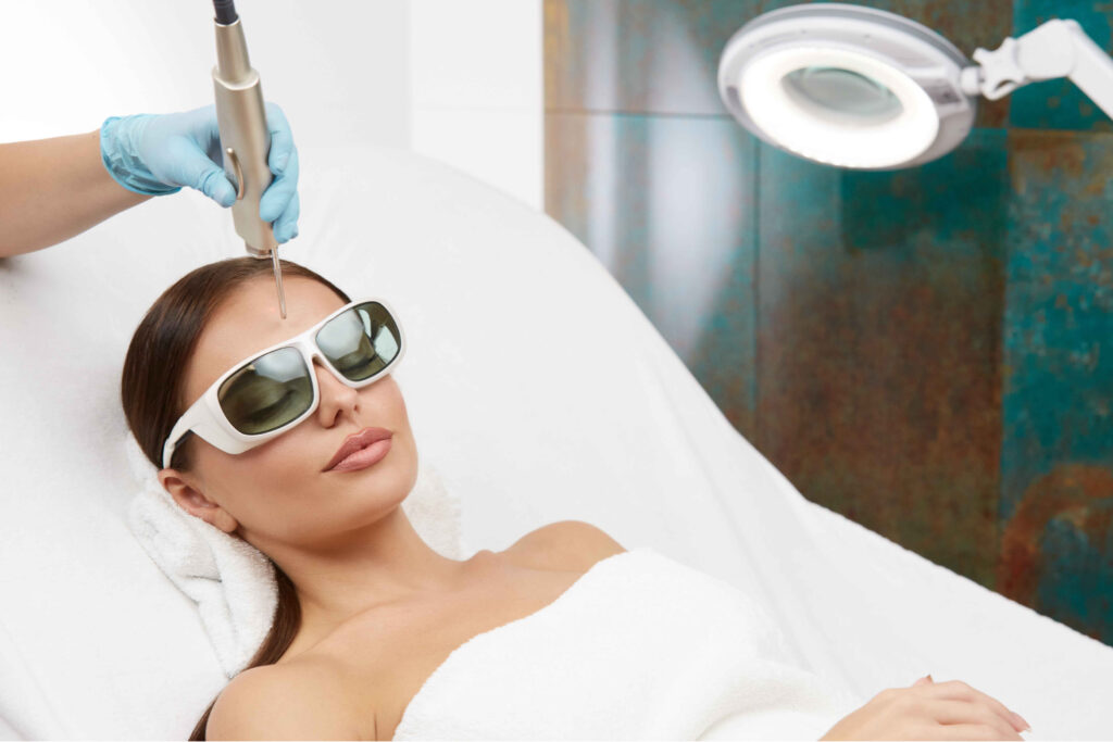 Beautiful Laying Woman Wearing Safety Goggles & Getting Center Brow Laser Hair Removal Treatment | Aspen Prime MedSpa in Hoboken, NJ