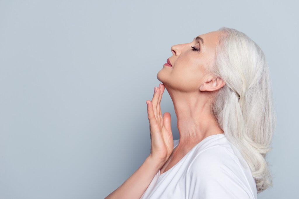 Old woman, touching her skin of neck with hand over grey background | Aspen Prime Med Spa in Hoboken, NJ