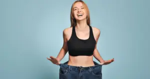 Woman showing loose jeans after successful weight loss in Hoboken, NJ, highlighting a slimmer and healthier figure.